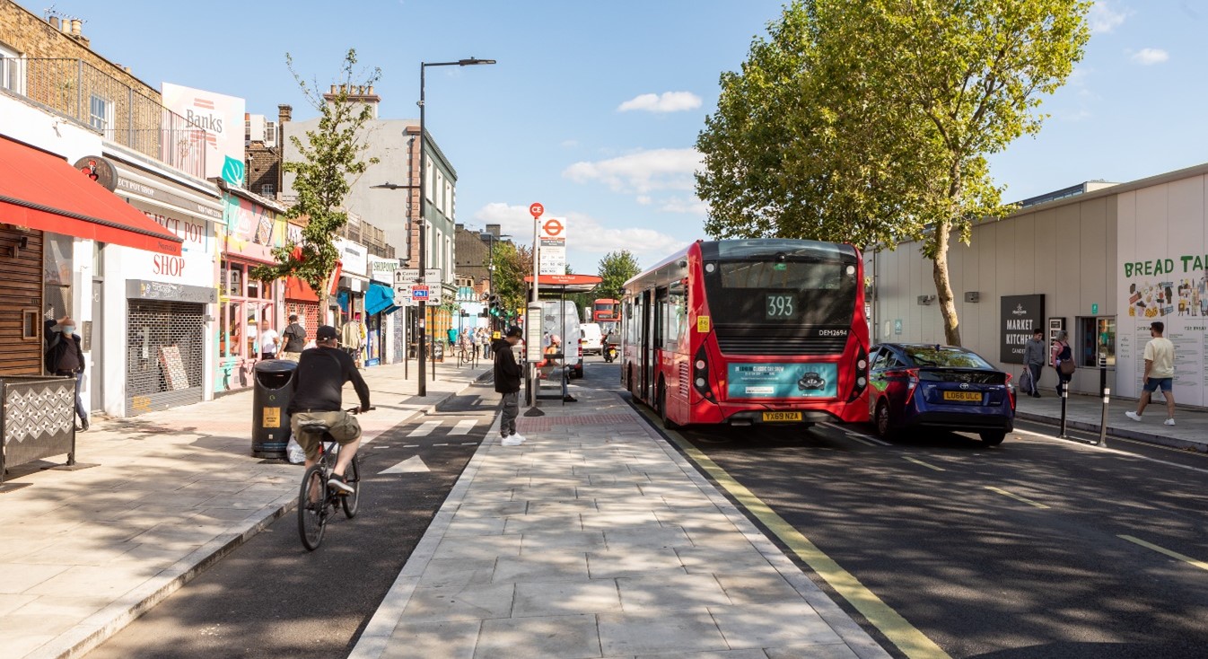 Image of road with a separate cycle lane, pedestrian island with bus stop shelter and main road with bus waiting at bus stop.