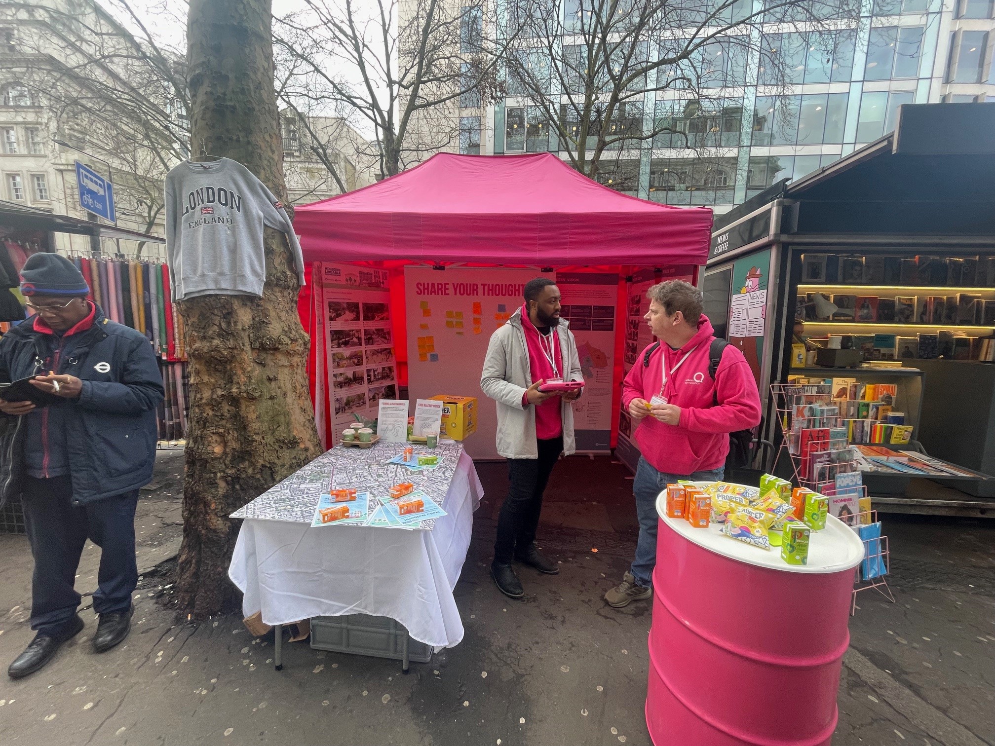 IMage of a pink tent with display boards and maps and two people with pink clothes talking