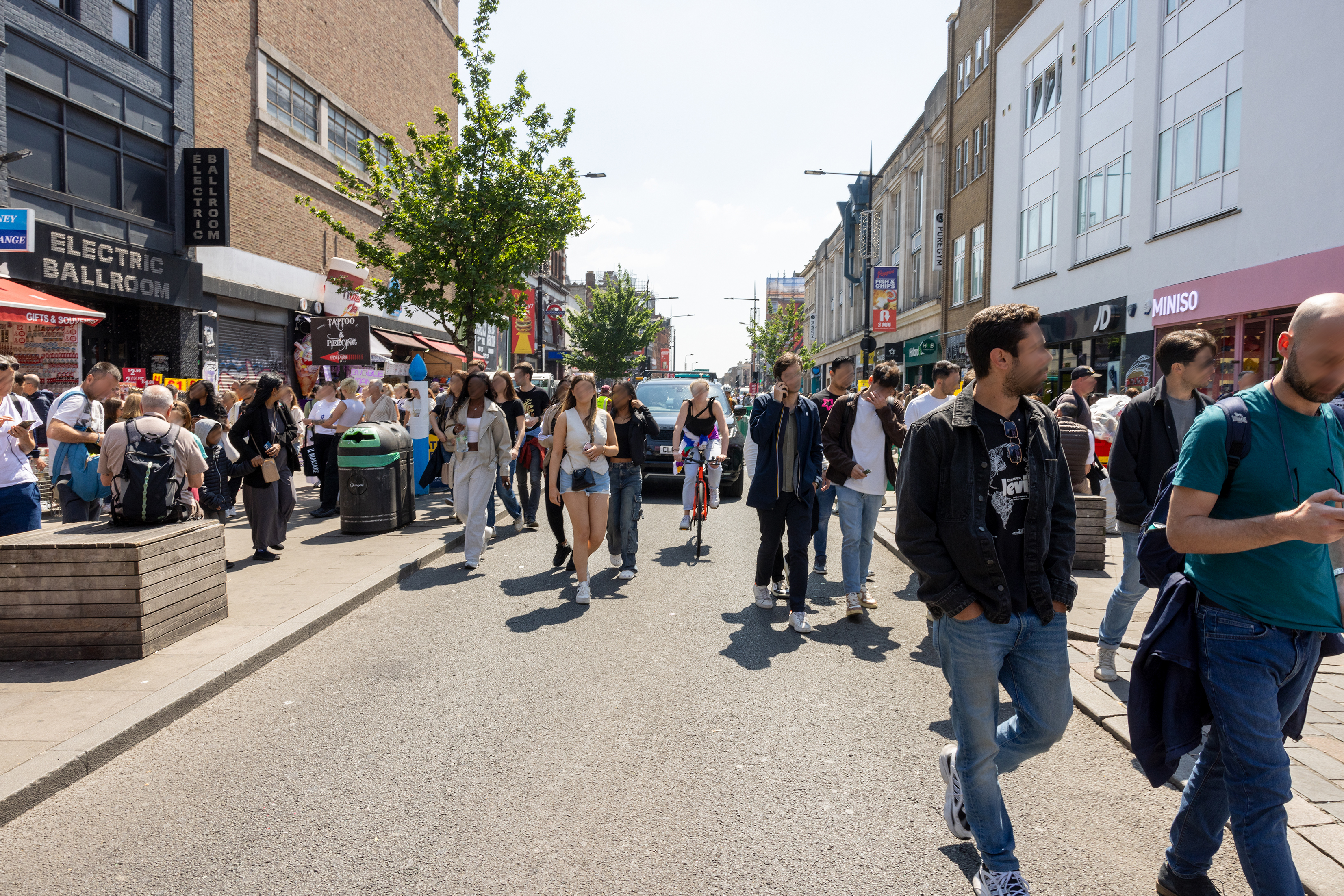 Image of a crowded section of Camden High Street with people walking in the street while a car and cyclist try ang get through