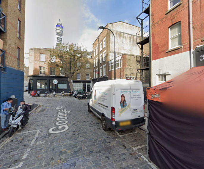 Goodge Place with motorbike parking and cobbled road surface and vehicles parked to the right