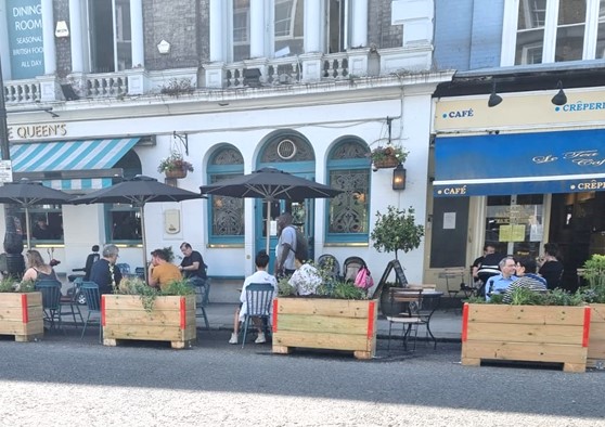 Image of people sitting at tables in the road in an area protected by barriers