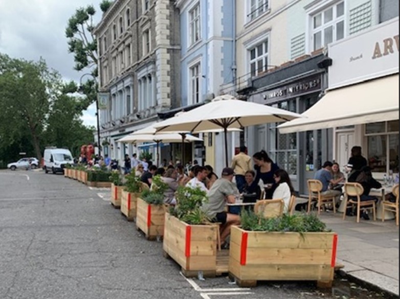 Image of people eating at tables in the road protected by planters