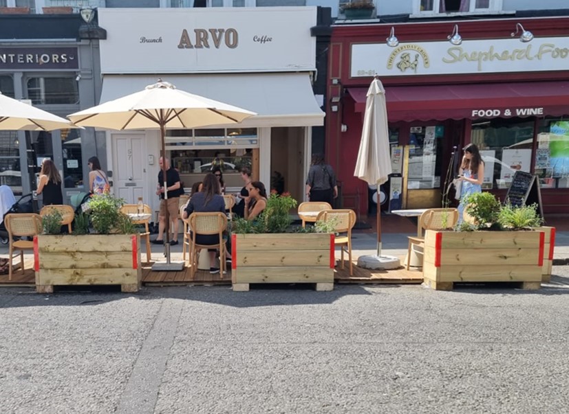 Image of people eating at tables in the road protected by planters